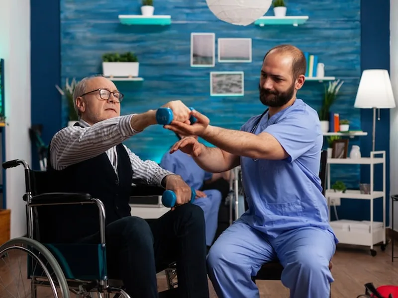 A therapist supporting an older man's arm as he lifts a light dumbbell during a seated therapy session