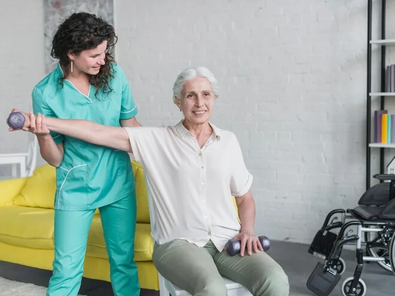A therapist guiding an older woman's arm out to the side with a light dumbbell