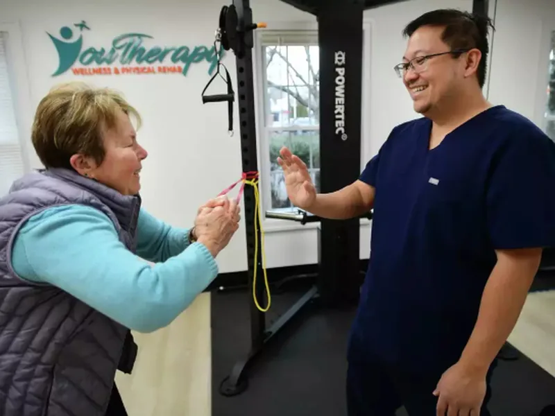 A therapist guiding an older woman through a resistance band exercise in the Youtherapy gym in Milford